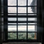 A classic window frame with a view of scenic hills and lush landscape, casting soft daylight indoors.