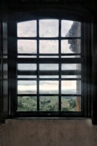 A classic window frame with a view of scenic hills and lush landscape, casting soft daylight indoors.
