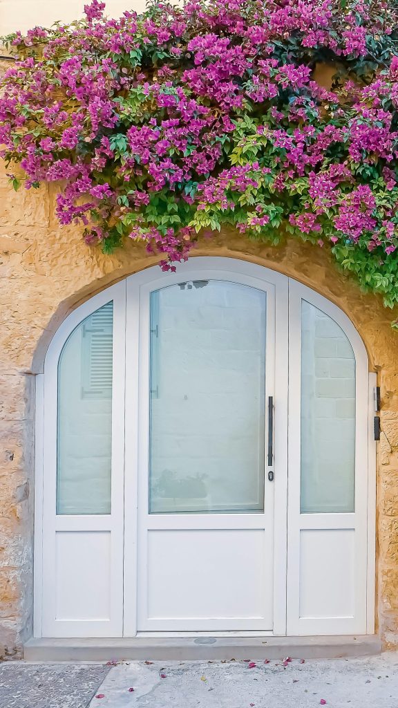A picturesque Maltese doorway adorned with vibrant bougainvillea in a sunny, peaceful setting.
