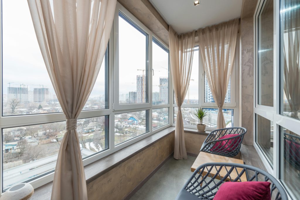 Interior of spacious patio in multistory building with chair and table placed in front of big windows in daytime
